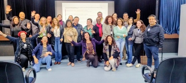 Fotografia com 24 pessoas em pé e agachadas posando, ao fundo, uma projeção em slides,